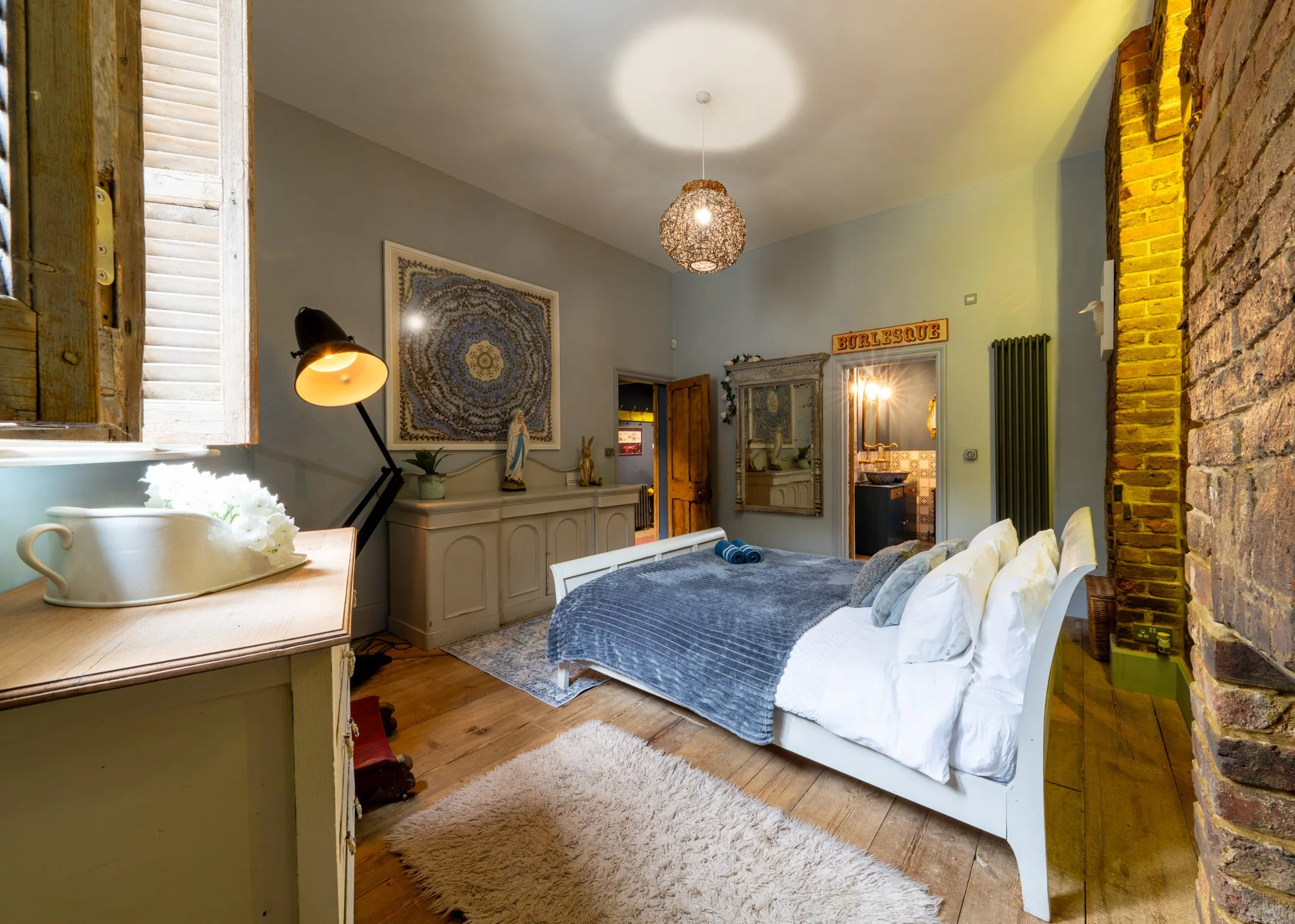 The guest bedroom at The Bath House — exposed brick wall, eclectic vintage furnishings and king bed